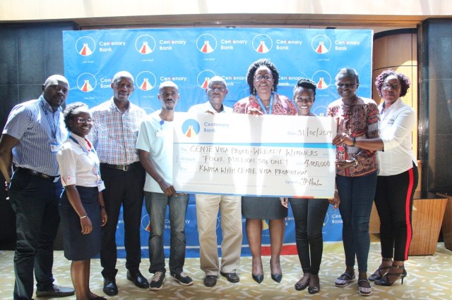 Beatrice Lugalambi (4th R), Centenary Bank’s General Manager, Corporate Communication & Marketing hands over a dummy cheque worth UGX 4 million to its customers and  staff as a reward for transacting using their Cente Visa card across the different digital platforms at least 4 times a week under the 'Kwasa with CenteVisa' promotion.